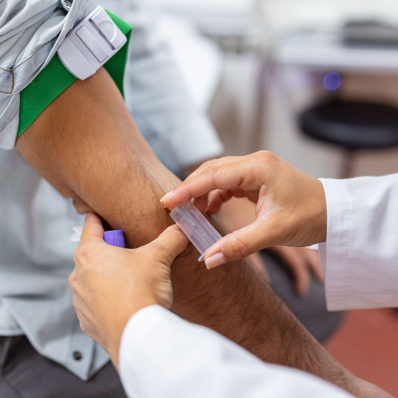 Un professionnel de la santé prélève du sang au bras d'un patient à l'aide d'une seringue dans un environnement clinique.
