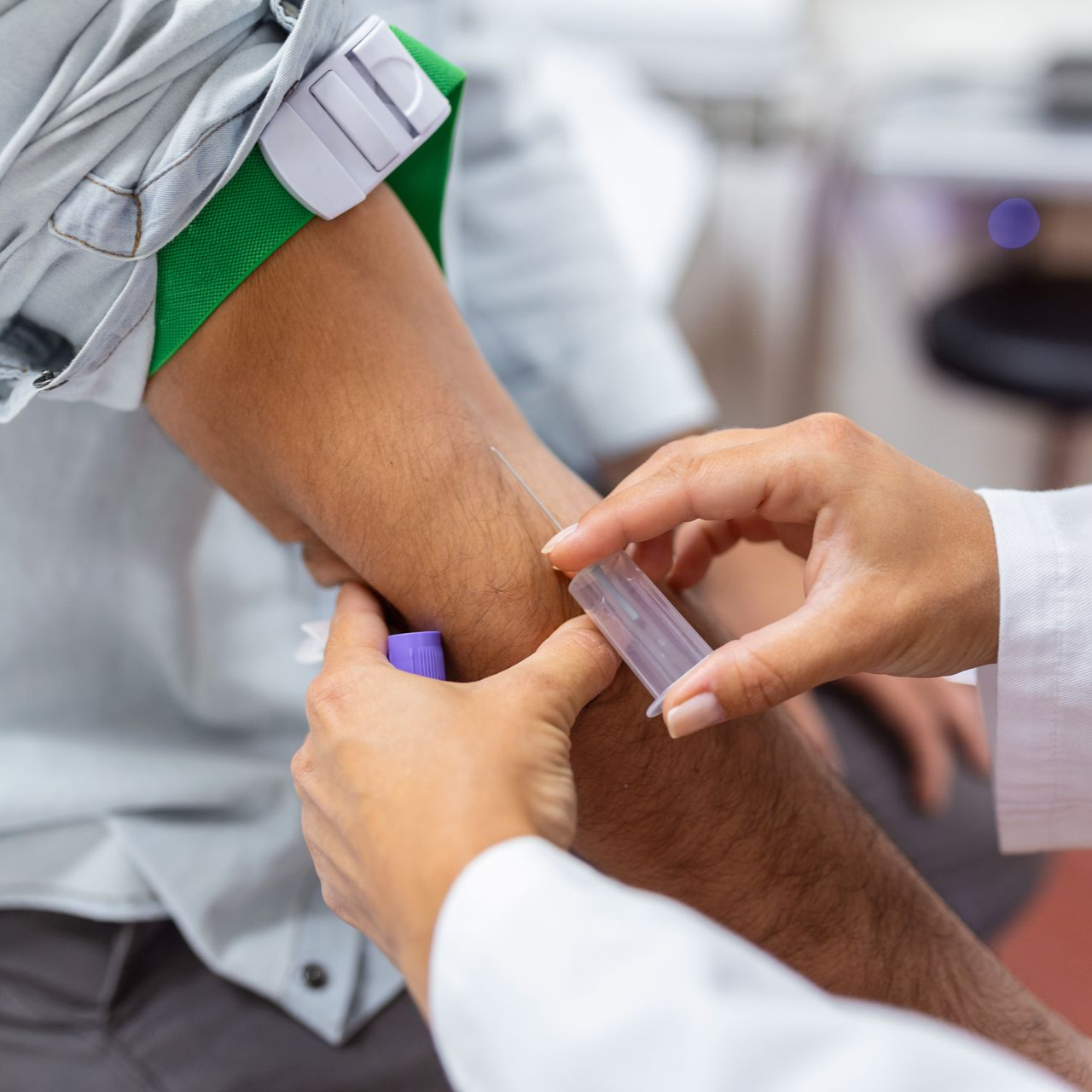 Prélèvement sanguin effectué sur le bras d'un patient à l'aide d'une aiguille et d'un garrot.