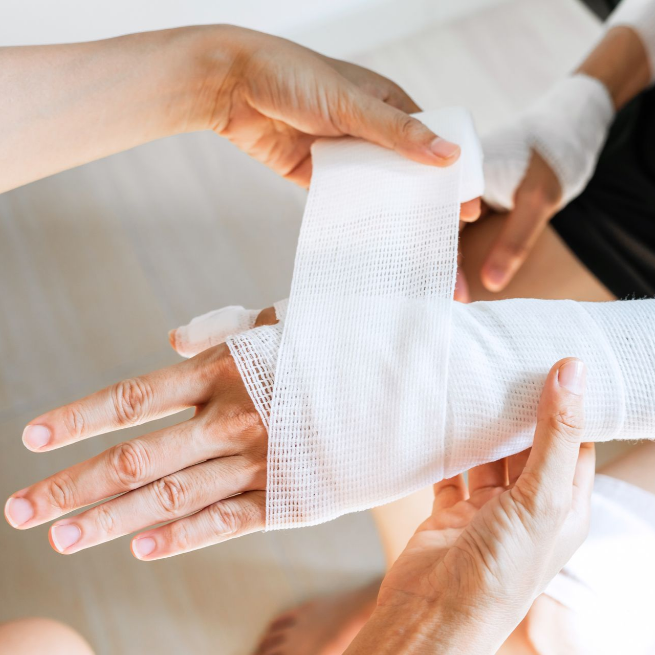 Des mains enroulent un bandage de gaze blanche autour d'un poignet et d'une paume.