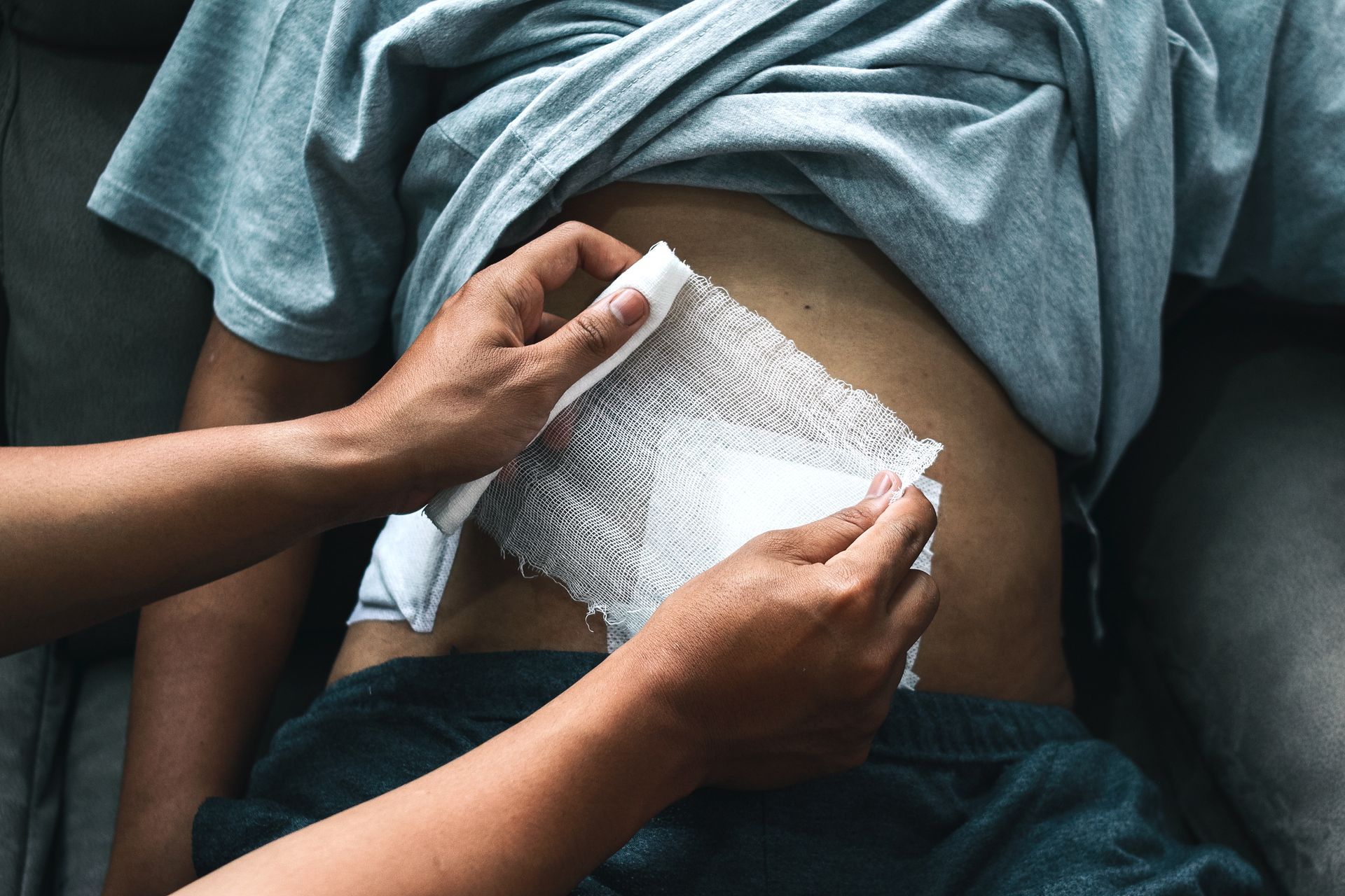 Des mains appliquent un bandage blanc sur l'abdomen d'un homme.