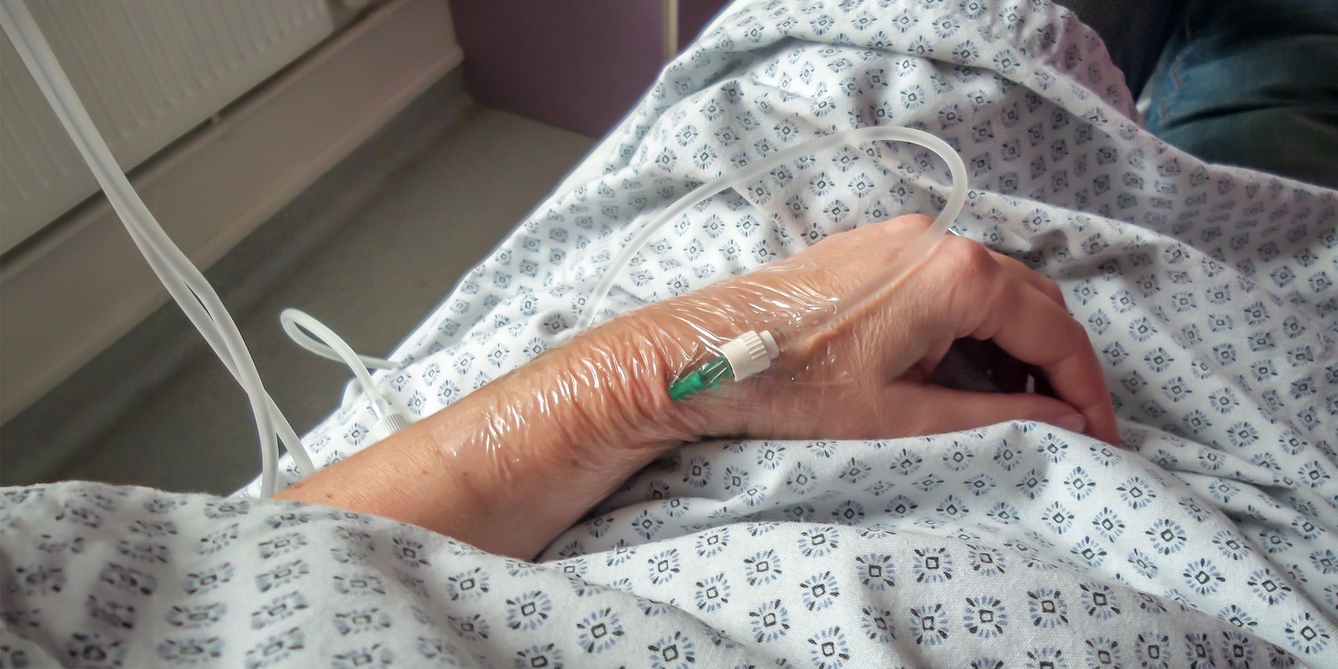 Lit d'hôpital avec la main perfusée d'un patient reposant sur une couverture à motifs.