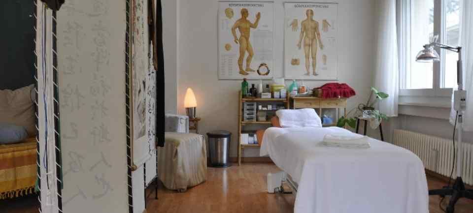 Une salle de massage avec un lit, des planches anatomiques et un lampadaire.