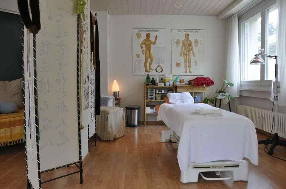 Salle de massage avec table de traitement, planches anatomiques et lampe chauffante.