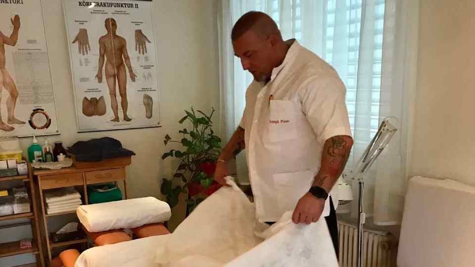 Un homme en blouse blanche prépare une table de massage dans une salle de soins.