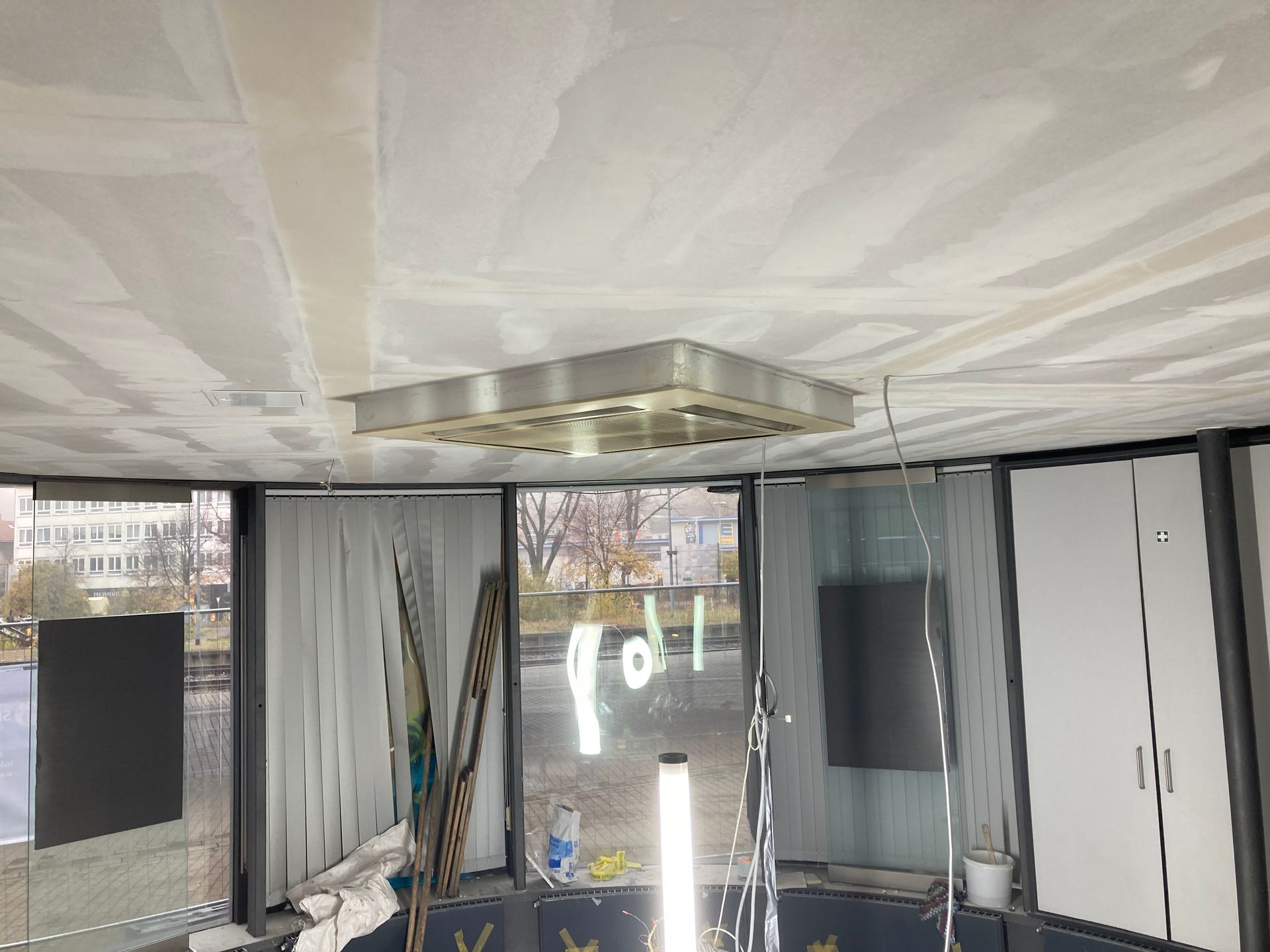 Decke mit Einbauleuchte in einem Raum mit großen Fenstern, unverputzten Trockenbauwänden und Wasserblick.