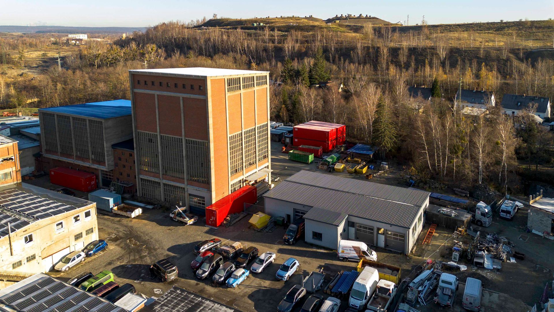 Großes Industriegebäude aus Backstein, diverse kleinere Gebäude und geparkte Fahrzeuge im Freien.
