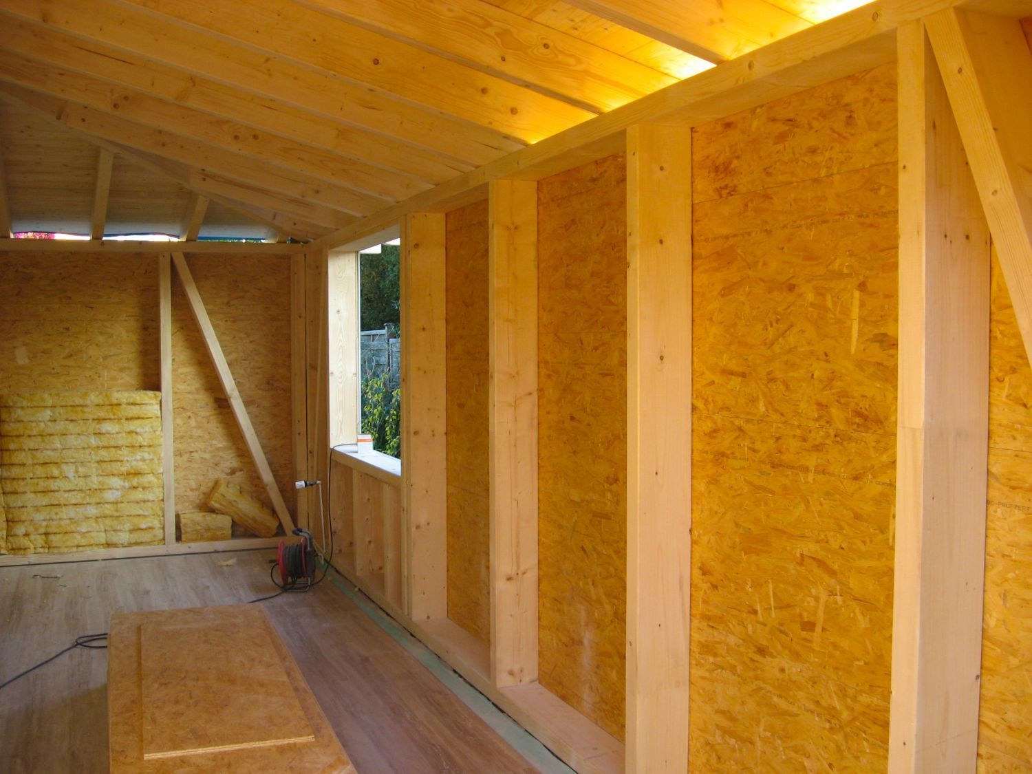 Innenansicht eines im Bau befindlichen Holzgebäudes mit freiliegenden Balken und OSB-Wandplatten.