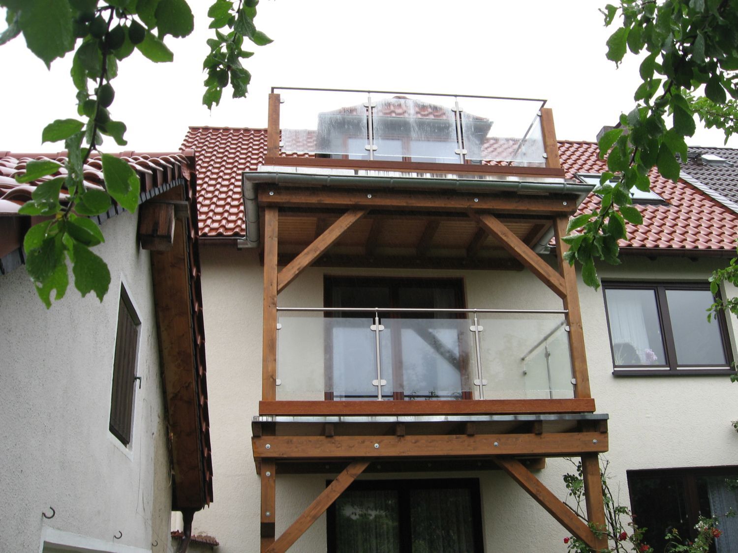 Holzbalkon mit Glasgeländer an einem zweistöckigen Gebäude; bedeckter Himmel.