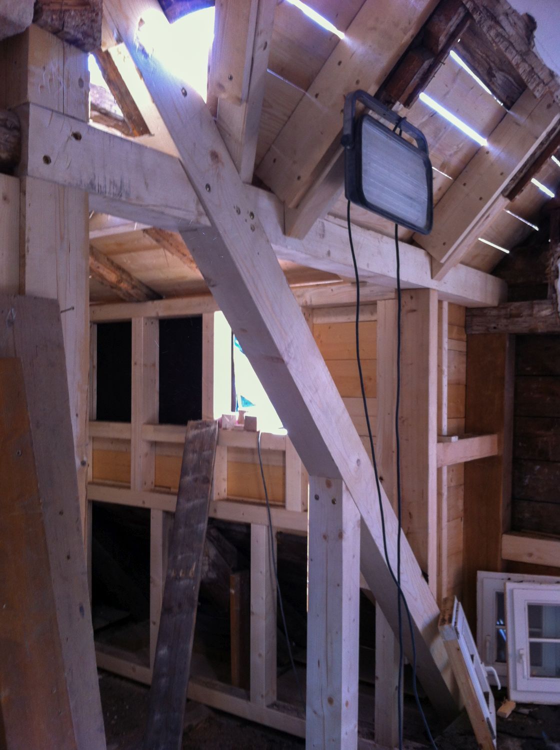 Innenansicht eines im Bau befindlichen Gebäudes mit freiliegenden Holzbalken, einer Lampe und unfertigen Wänden.
