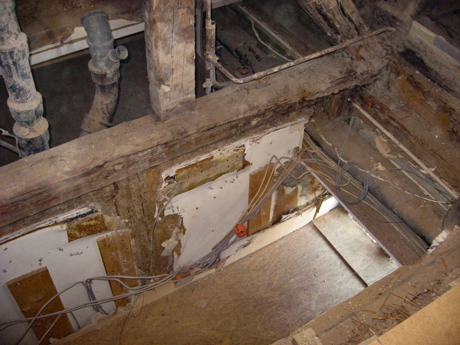 Freiliegende Holzbalken und Rohre; beschädigte Wände und Fußböden im Umbau.