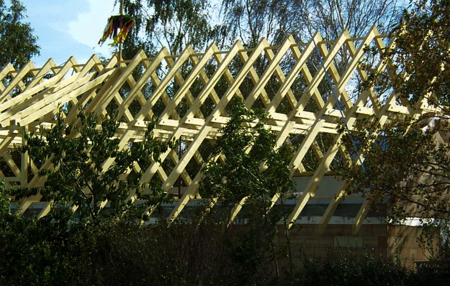 Auf einem Gebäude werden hölzerne Dachstühle errichtet, eine Person arbeitet obenauf.