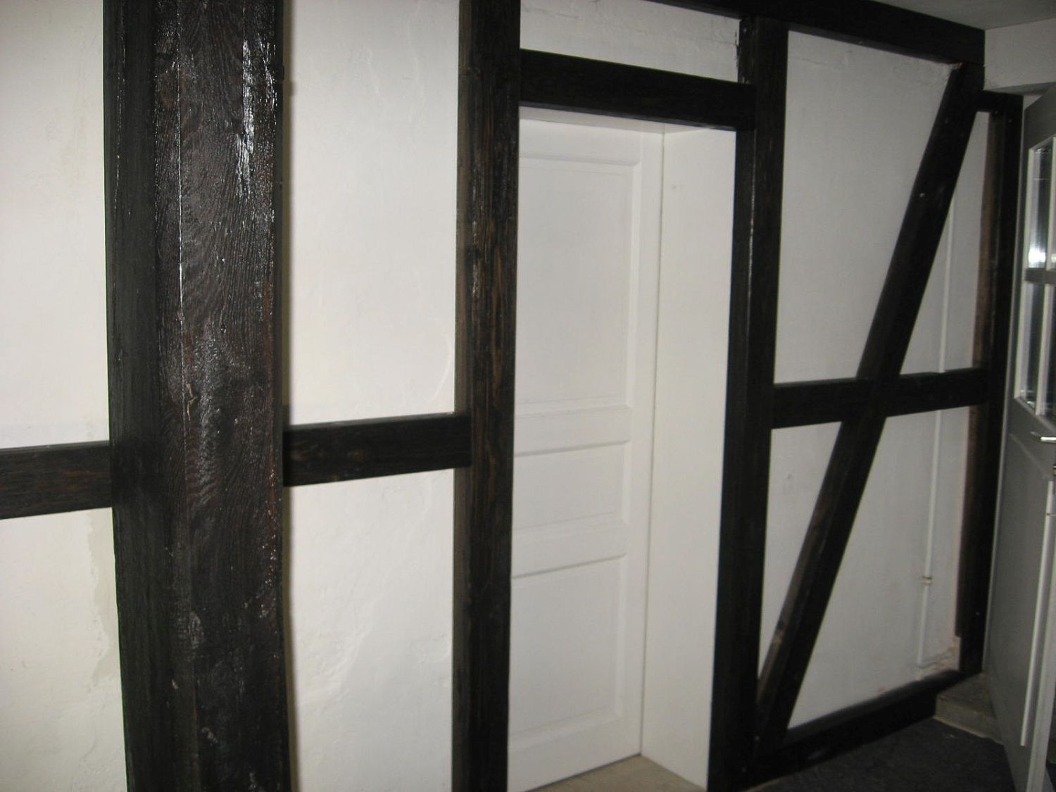 Dunkle Holzbalken bilden einen Rahmen um weiße Wände und eine weiße Tür in einem Zimmer.