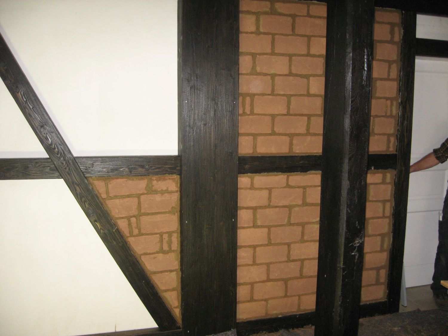 Wand aus Ziegeln und Fachwerk, mit schwarzen Balken und cremefarbener Ziegelfüllung.