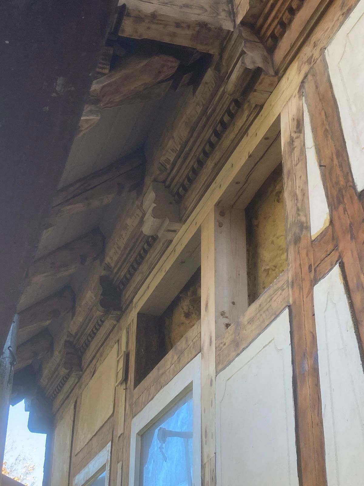 Nahaufnahme der Fachwerkfassade eines Gebäudes mit dekorativen Holzarbeiten und freiliegenden Balken mit Fenstern.