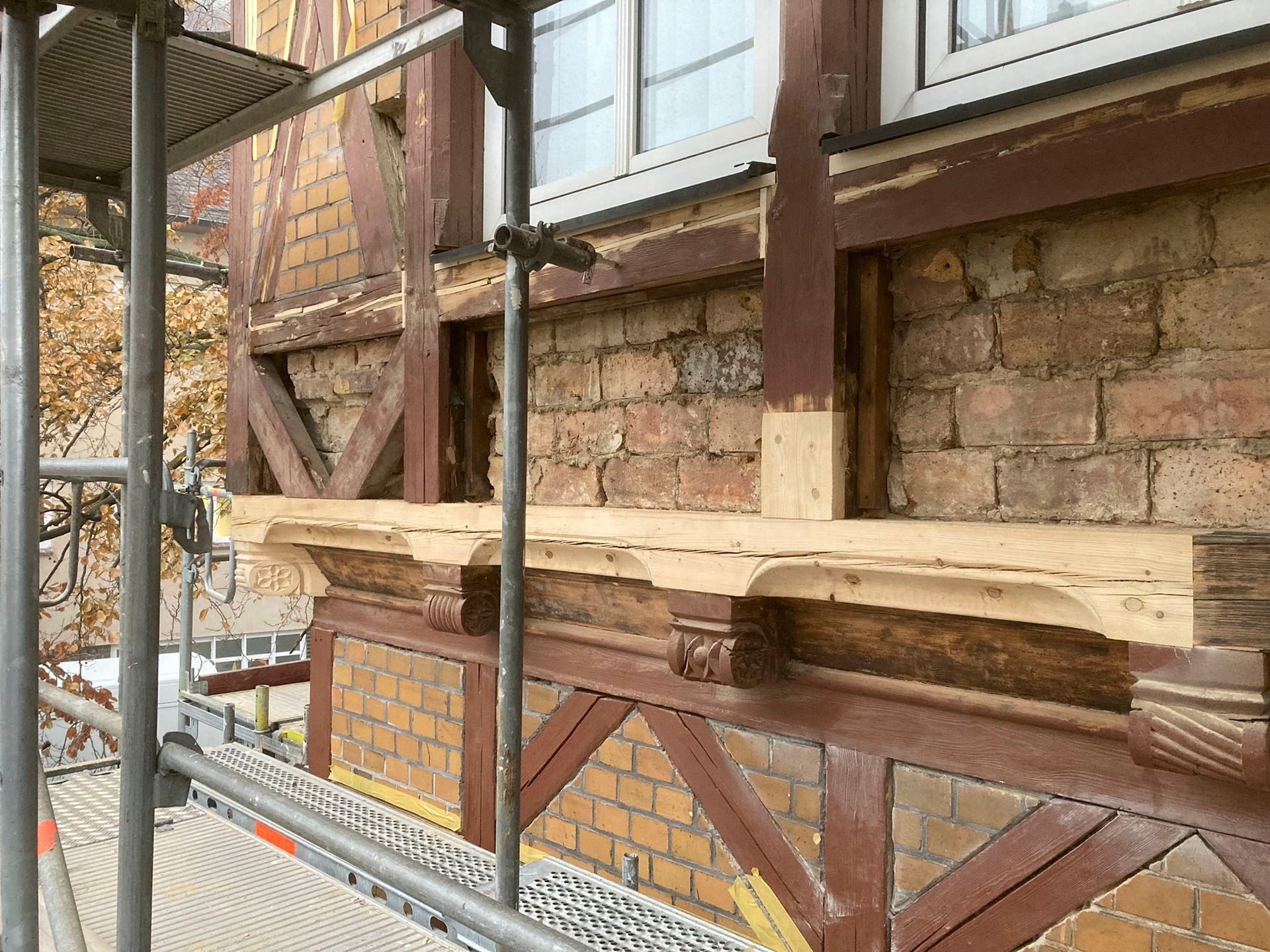 Außenansicht eines Gebäudes im Umbau mit freiliegenden Ziegelsteinen, braunen Balken und Gerüst.