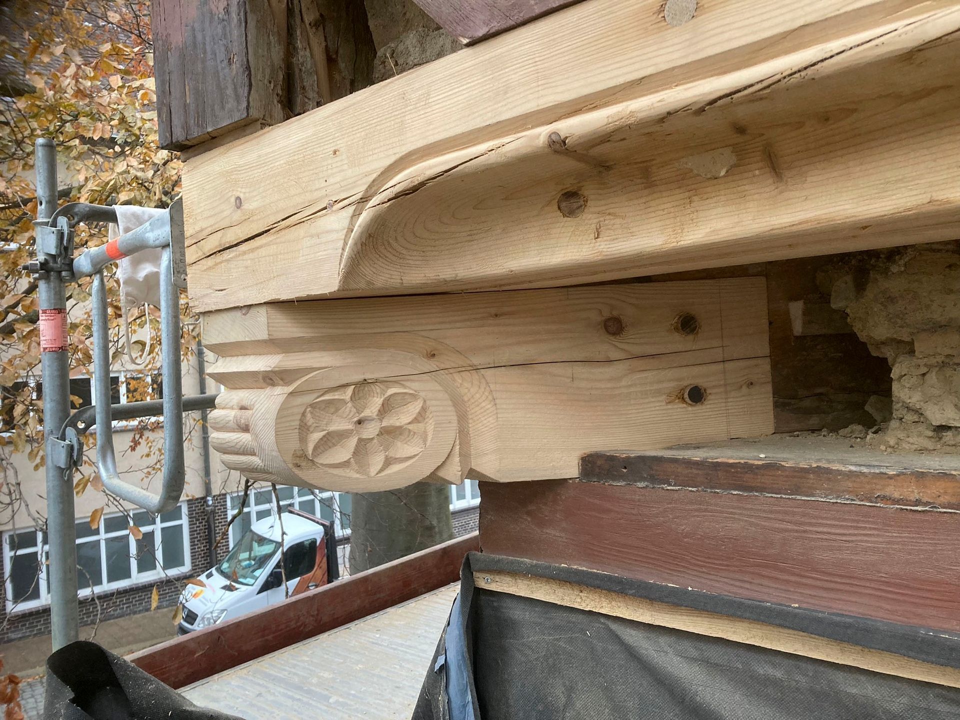 Nahaufnahme einer geschnitzten Holzkonsole mit aufwendigem Blumendekor, die ein Gebäudegesims stützt.