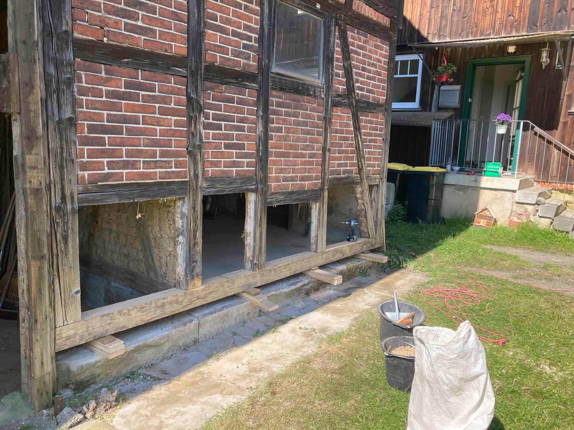 Außenansicht eines Fachwerk-Ziegelgebäudes, das derzeit renoviert wird. Die unterste Ziegelreihe fehlt und gibt den Blick ins Innere frei.