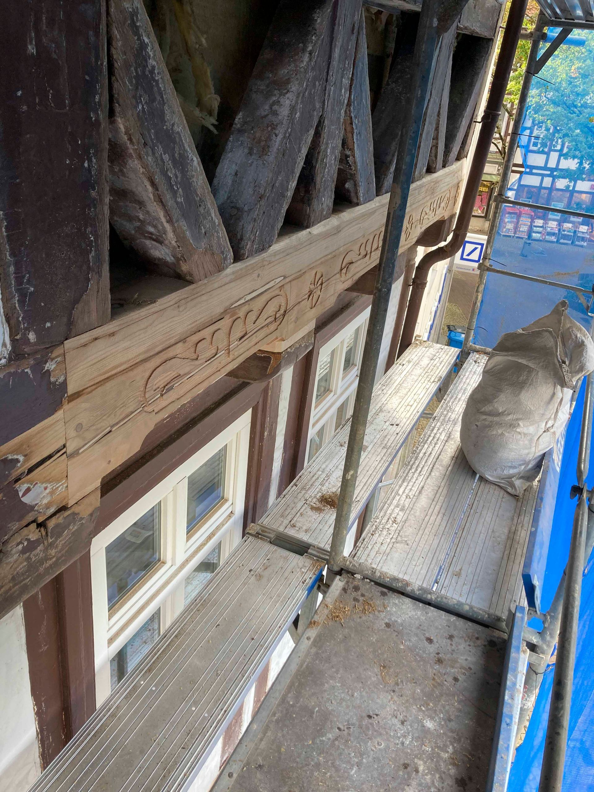 Aufwendige hölzerne Architekturelemente über Fenstern, Gerüsten und verwitterten Balken.