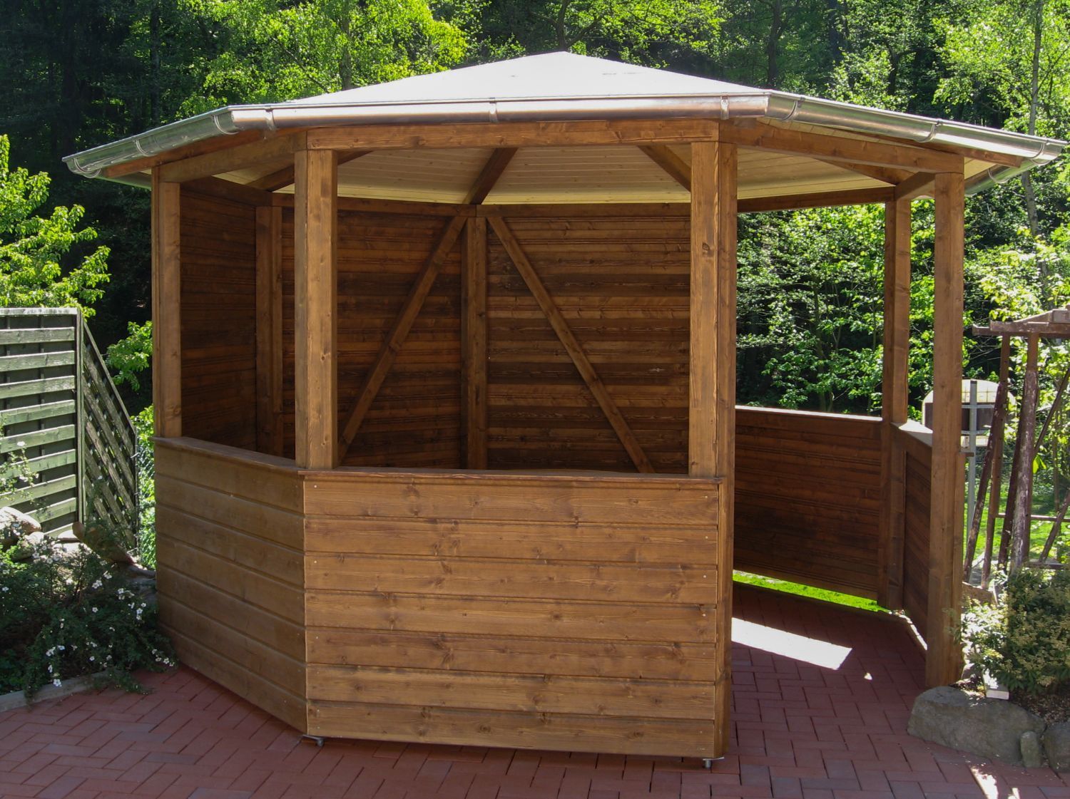 Holzpavillon mit weißem Dach in einer Gartenanlage.