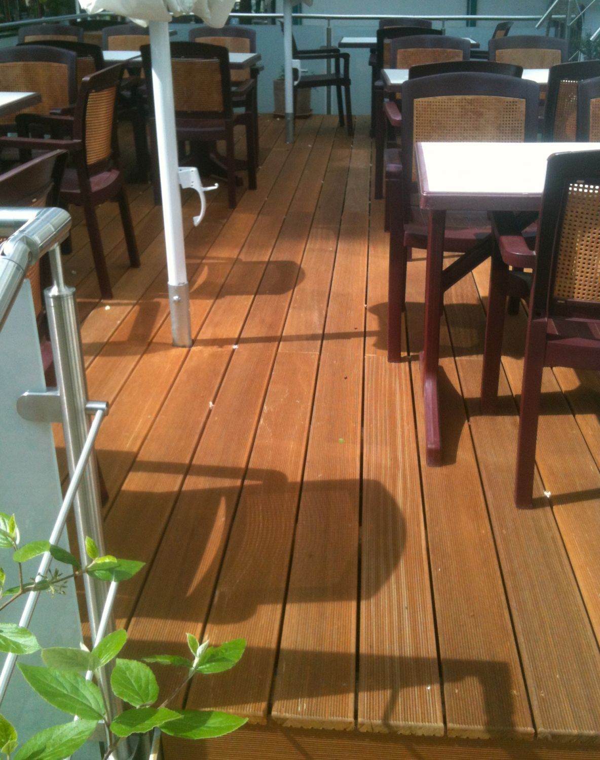 Holzterrasse mit Tischen und Stühlen unter einer Markise. Helles Sonnenlicht wirft Schatten.