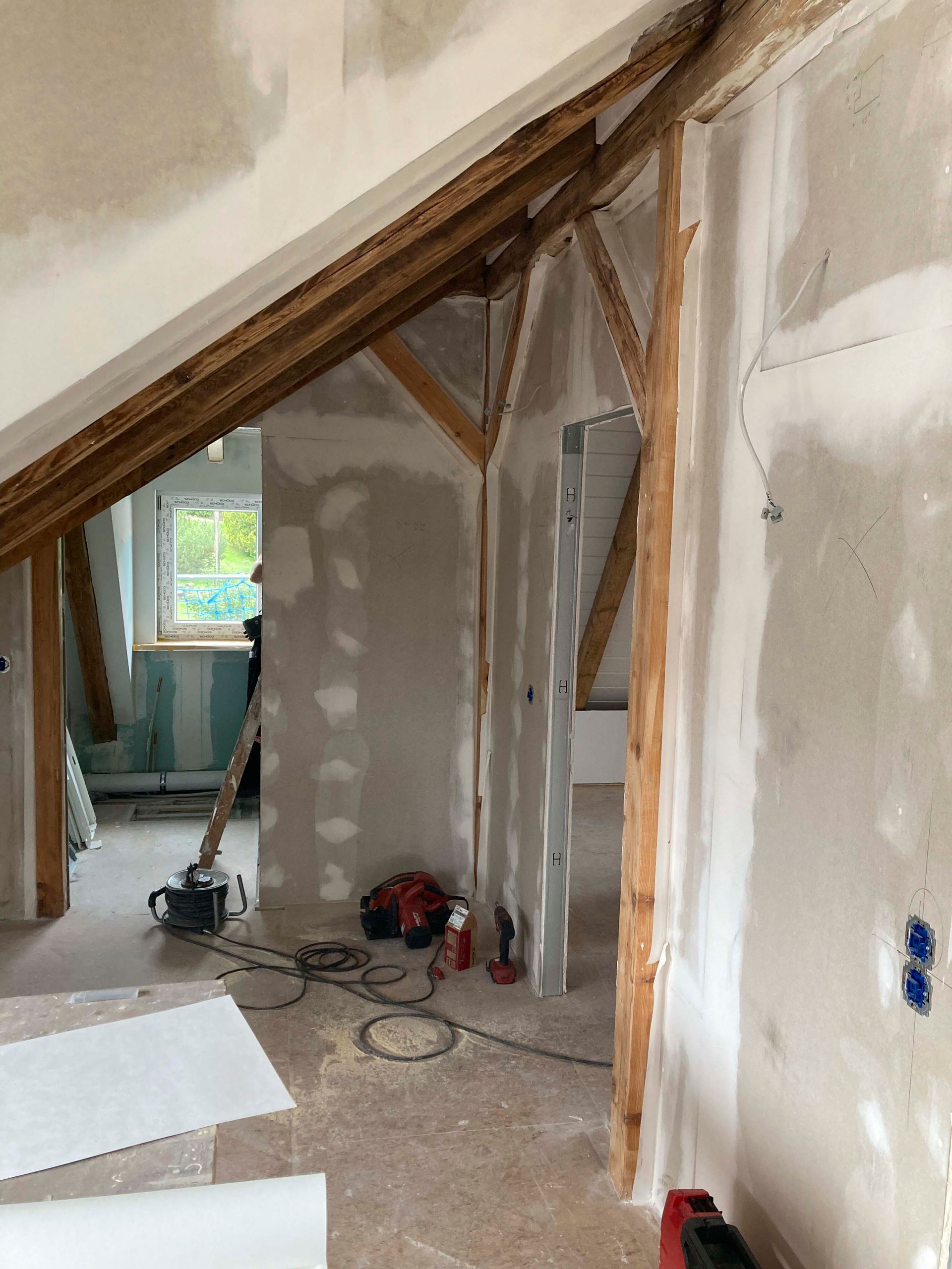 Innenräume im Bauzustand mit freiliegenden Holzbalken, Gipskartonwänden und herumliegenden Werkzeugen.