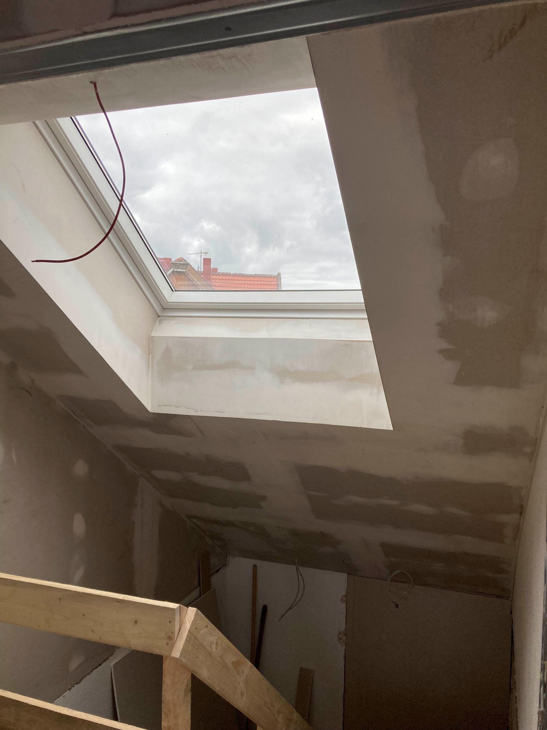Oberlicht in einem im Bau befindlichen Raum, von unten betrachtet, mit sichtbarem Treppenhaus und freiliegender Gipskartonwand.