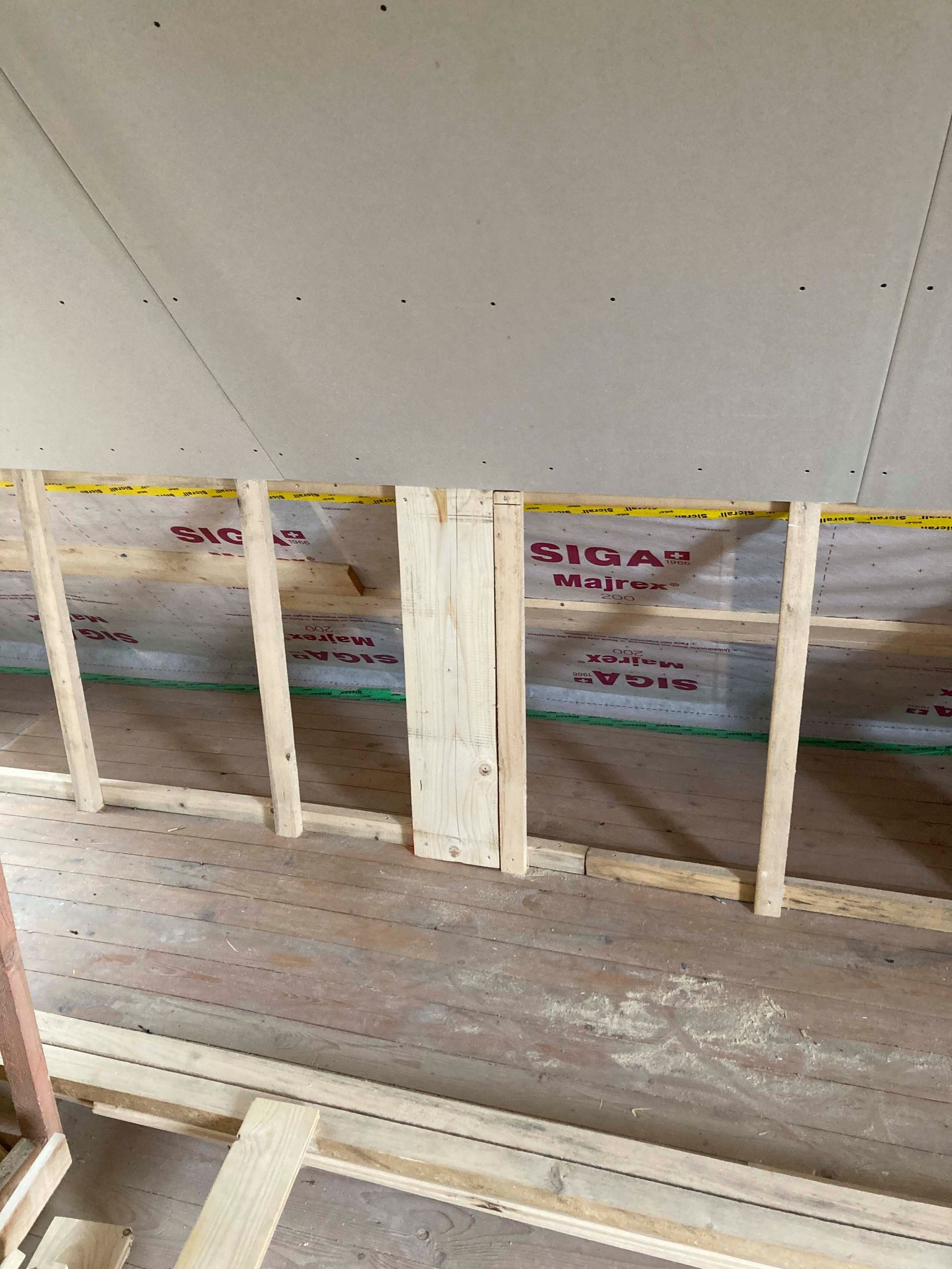 Innenansicht eines im Bau befindlichen Raumes mit freiliegenden Holzständern, Dämmung und Gipskartonwänden.