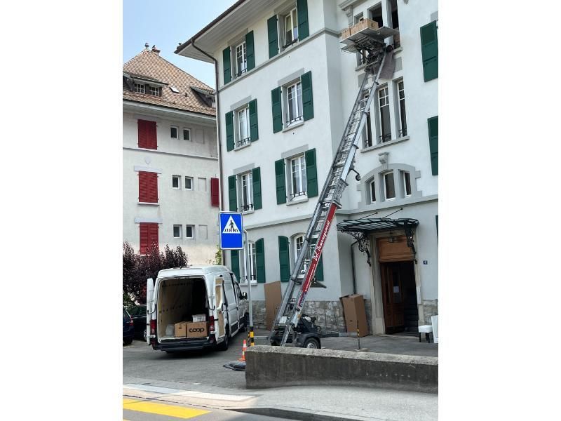 Une camionnette blanche est garée devant un bâtiment avec une échelle attachée dessus.