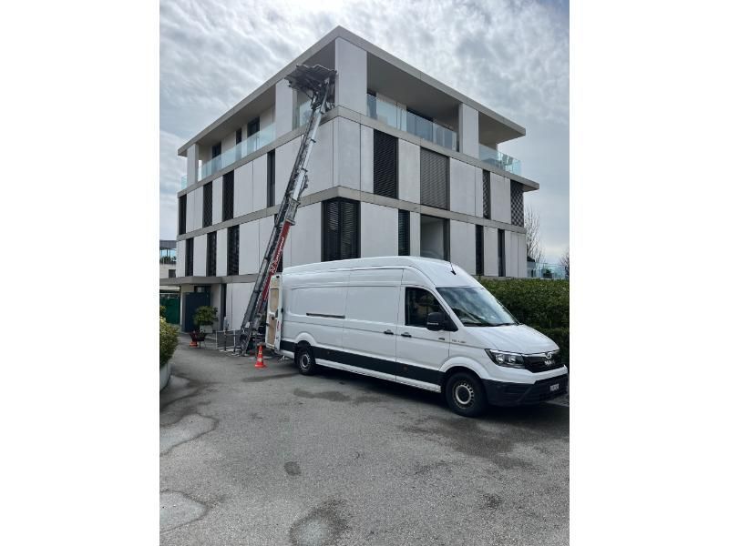 Une camionnette blanche avec une échelle attachée est garée devant un bâtiment.