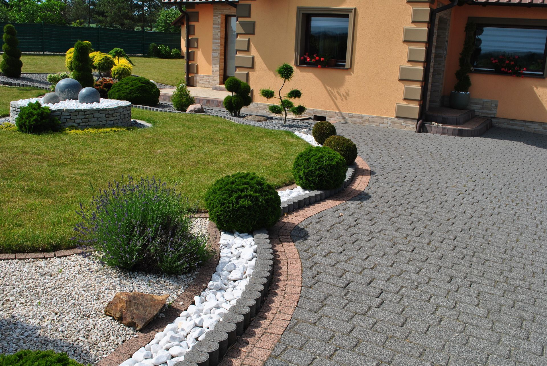 Allée gravillonnée bordée de buissons taillés devant une maison