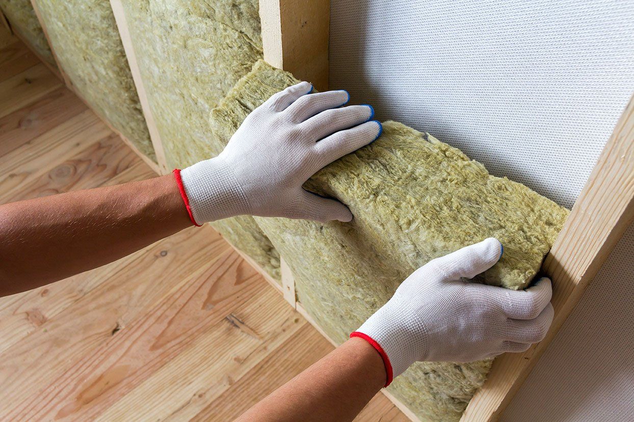 Focus sur les mains d'un homme qui pose des panneaux isolants au mur