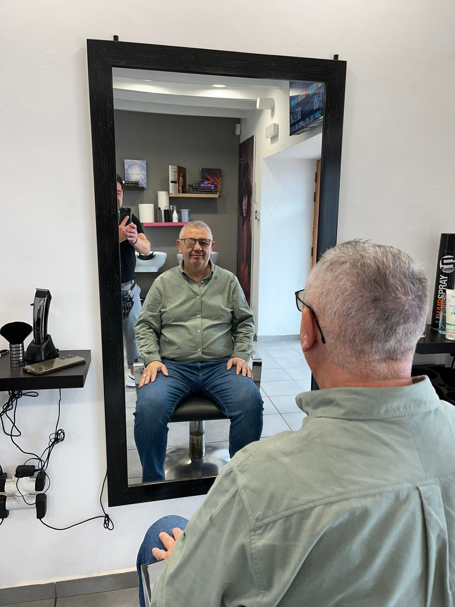 Un hombre está sentado frente a un espejo cortándose el pelo.