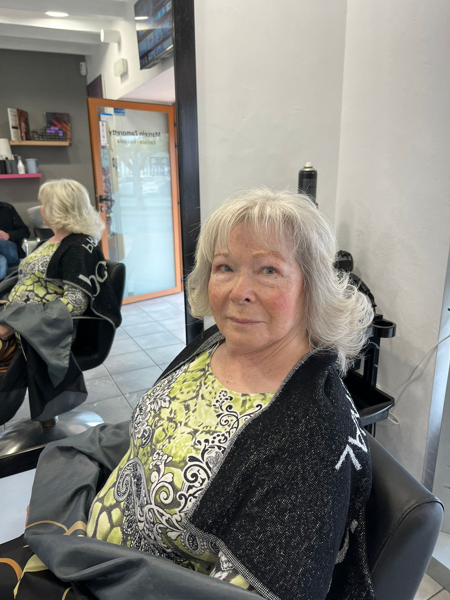 Una mujer mayor está sentada en una silla en una peluquería.