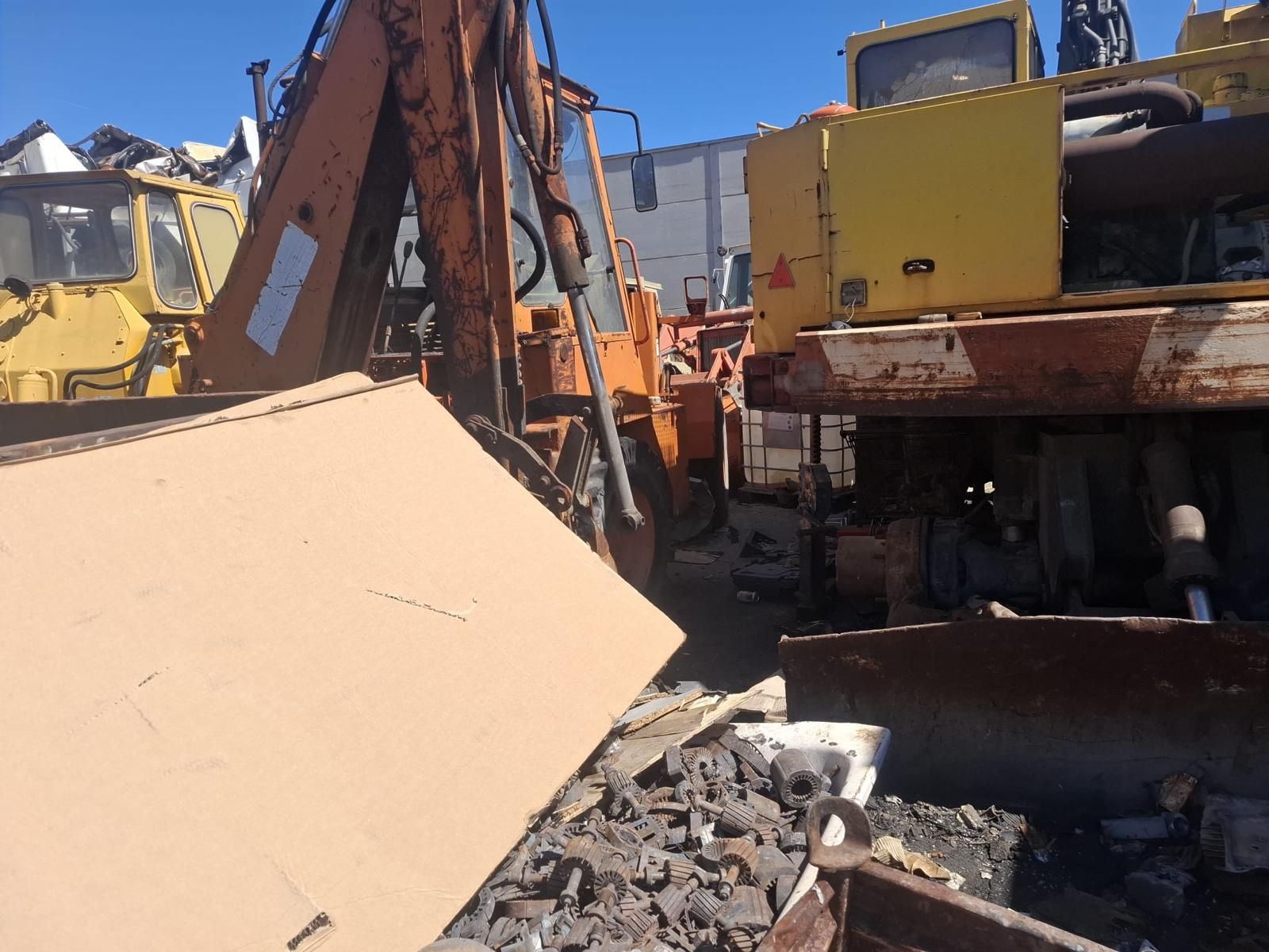 Un martillo hidráulico azul derriba escombros en una obra de demolición con edificios de apartamentos al fondo.
