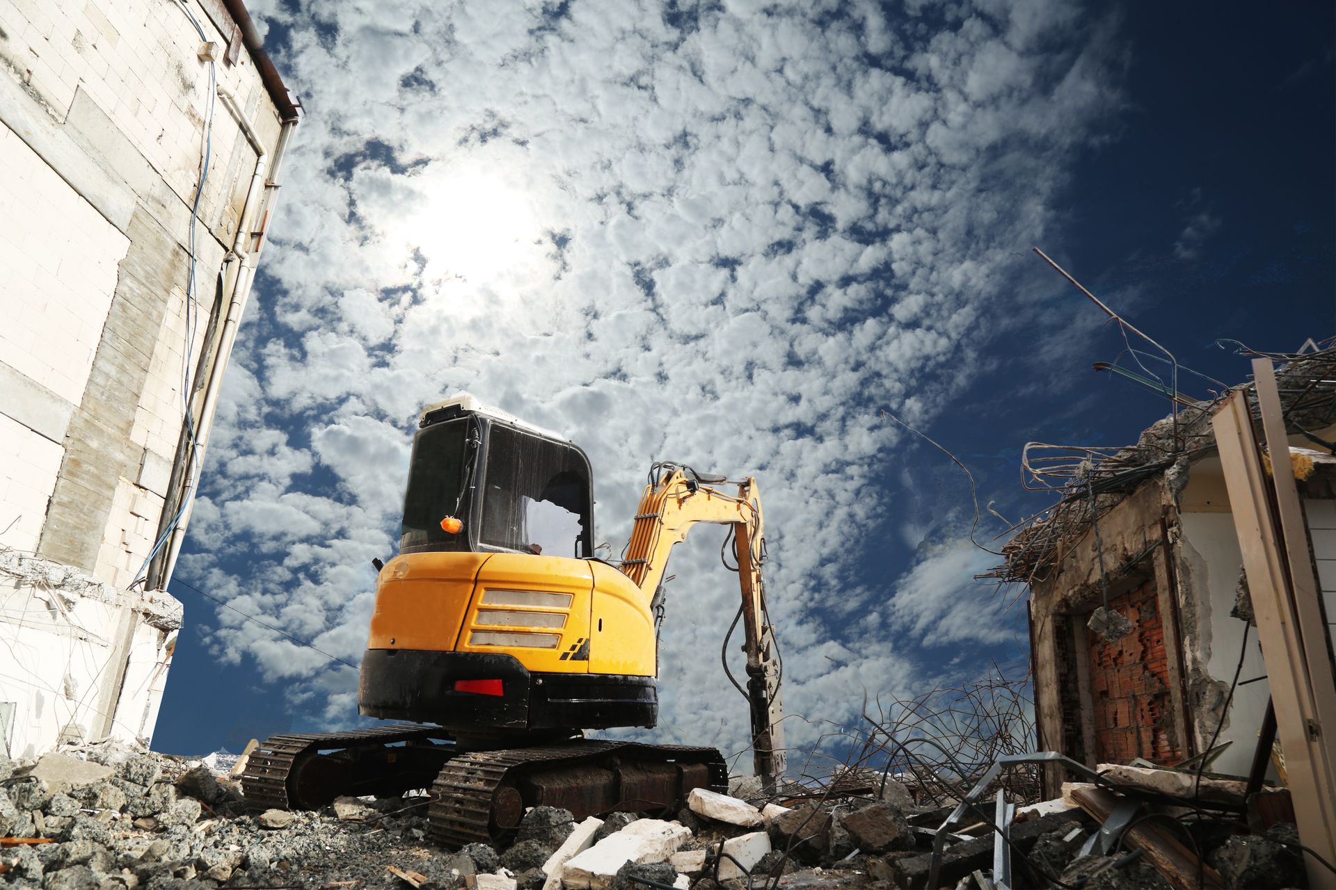 Excavadora amarilla entre escombros en un sitio de demolición bajo un cielo nublado.