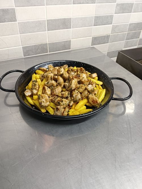 Una sartén llena de patatas y salchichas sobre una mesa.