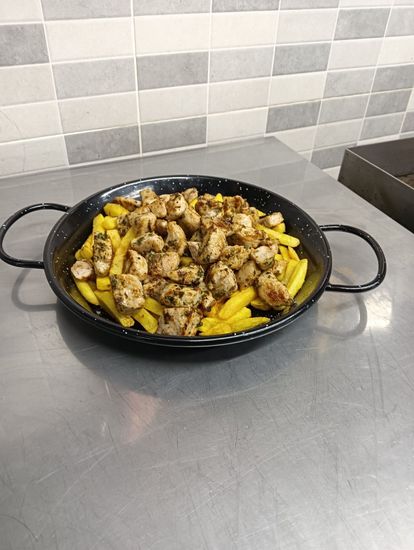 Una sartén llena de patatas y salchichas sobre una mesa.