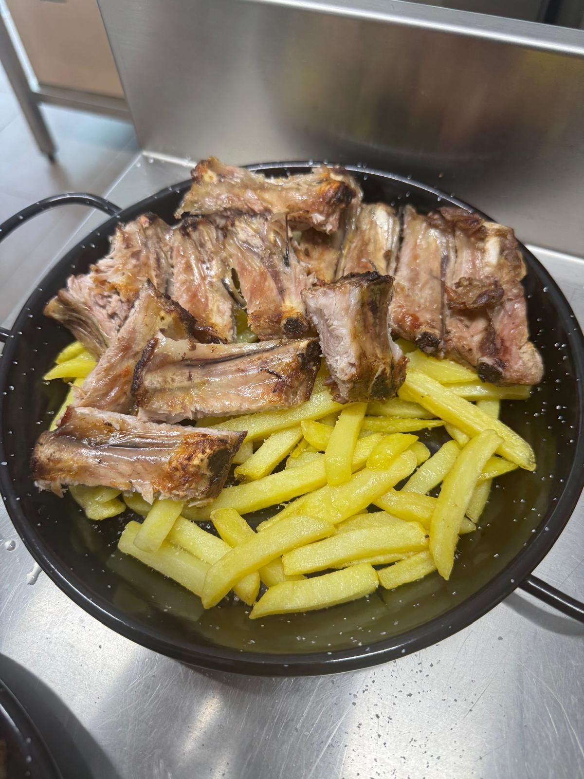 Una sartén llena de costillas y patatas fritas sobre una mesa.
