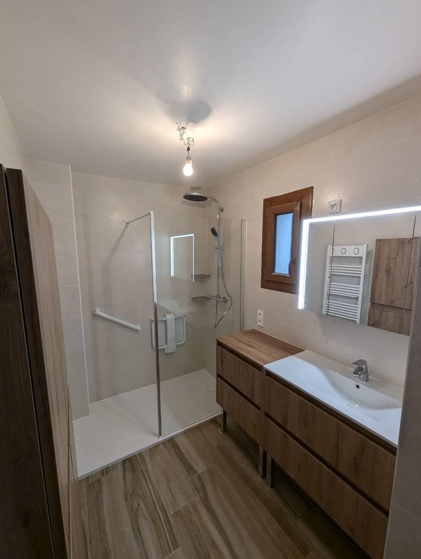 Salle de bains moderne avec sol imitation bois, cabine de douche, vanité et petite fenêtre avec porte-serviettes.