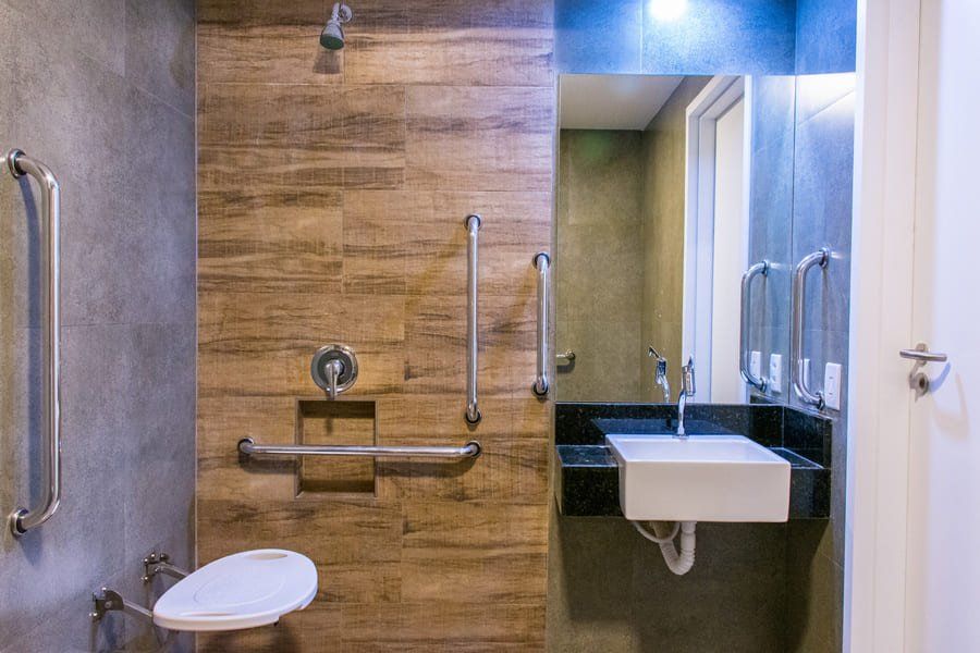 Salle de bains accessible avec douche, toilettes et lavabo. Barres d'appui et siège mural inclus.