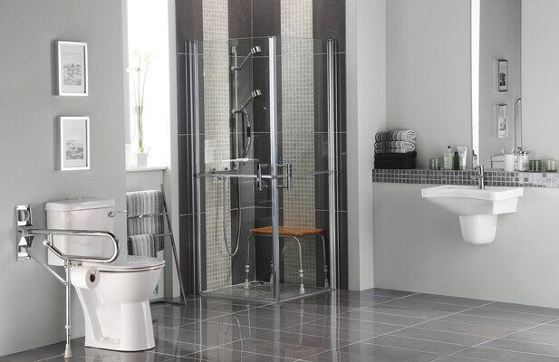 Salle de bains accessible avec toilettes, douche et lavabo. Robinetterie chromée. Carrelage gris, noir et blanc.
