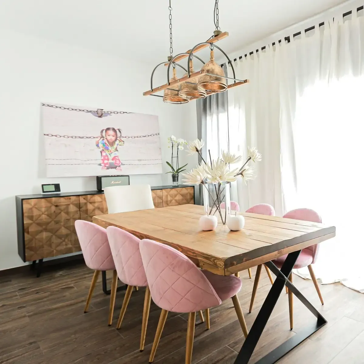 Comedor con mesa de madera, sillas rosas y lámpara de araña.