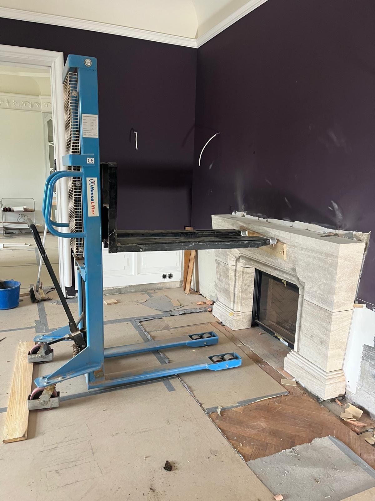 Blauer Aufzug neben einem Kamin während der Renovierung. Lila Wand und beschädigter Boden.