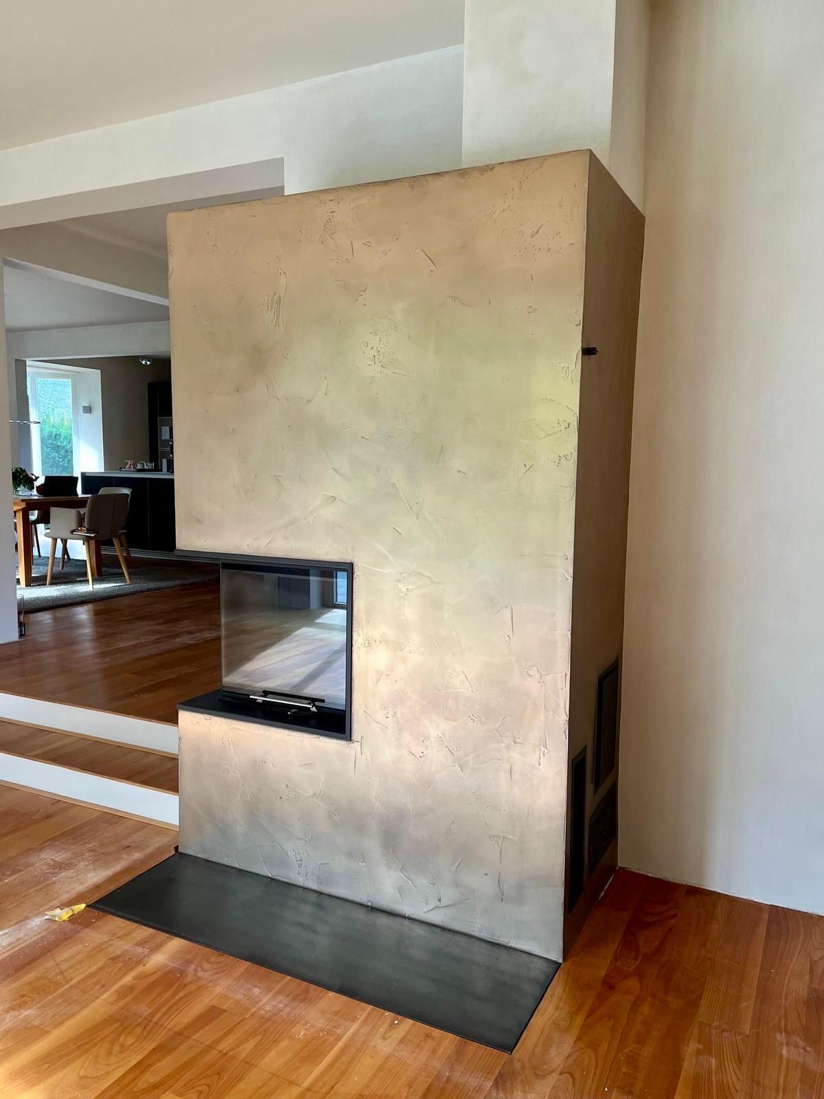 Moderner Kamin mit Metalloberfläche, Sichtfenster aus schwarzem Glas, auf Holzboden.