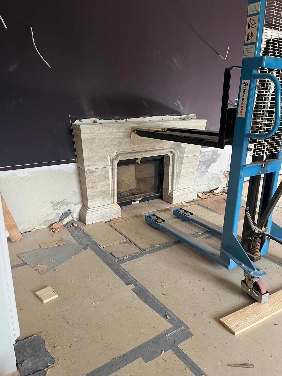 Ein Kamin wird mit einem blauen Gabelstapler versetzt. Der Kamin besteht aus hellem Stein und hat eine dunkle Öffnung.