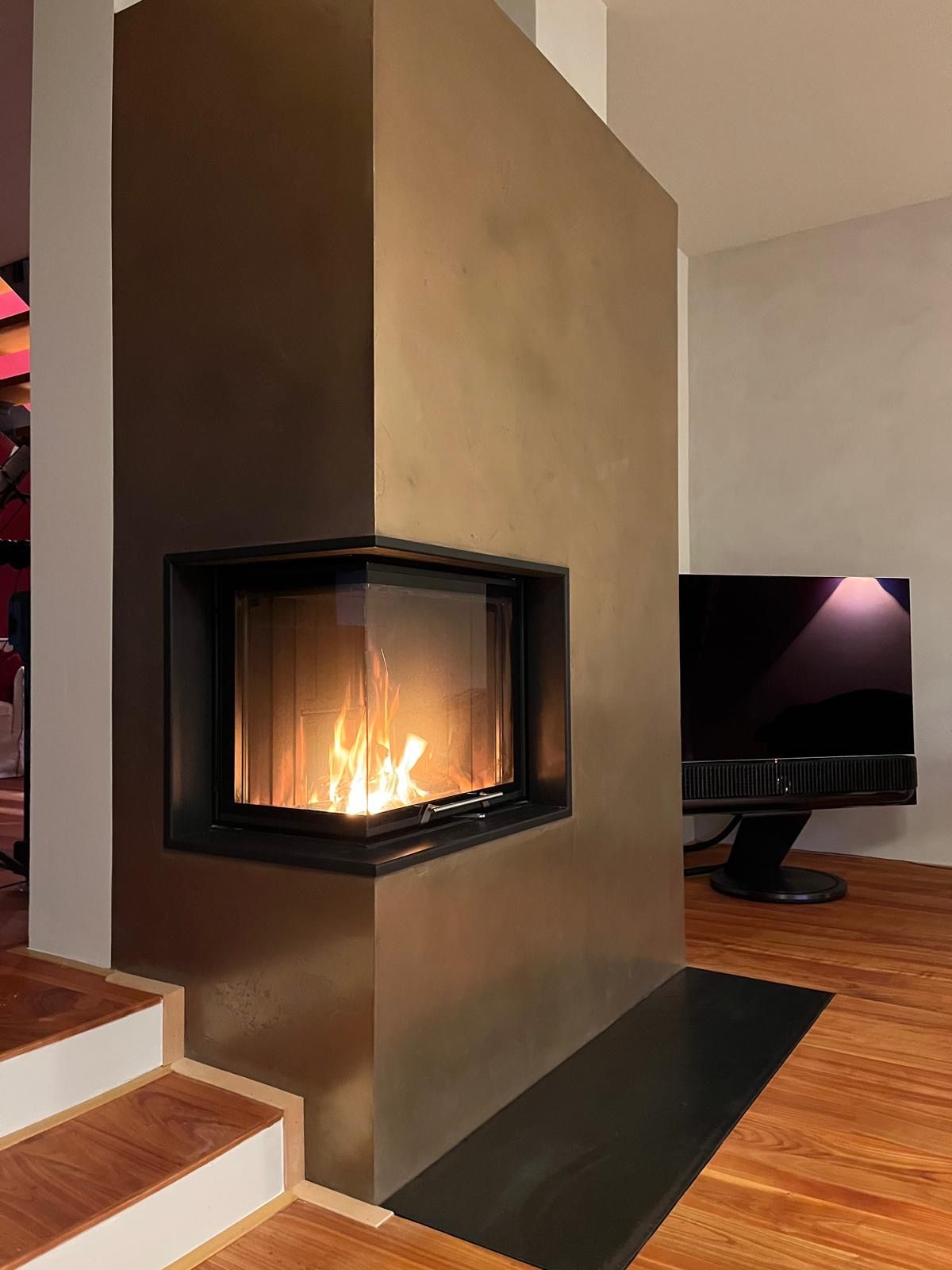 Eckkamin mit Flammen, braune, strukturierte Wand, Holzboden und ein Fernseher.