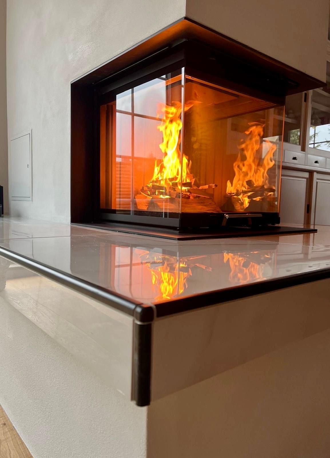 Ein Feuer brennt in einem modernen, verglasten Kamin, der in eine weiße Arbeitsplatte eingelassen ist.