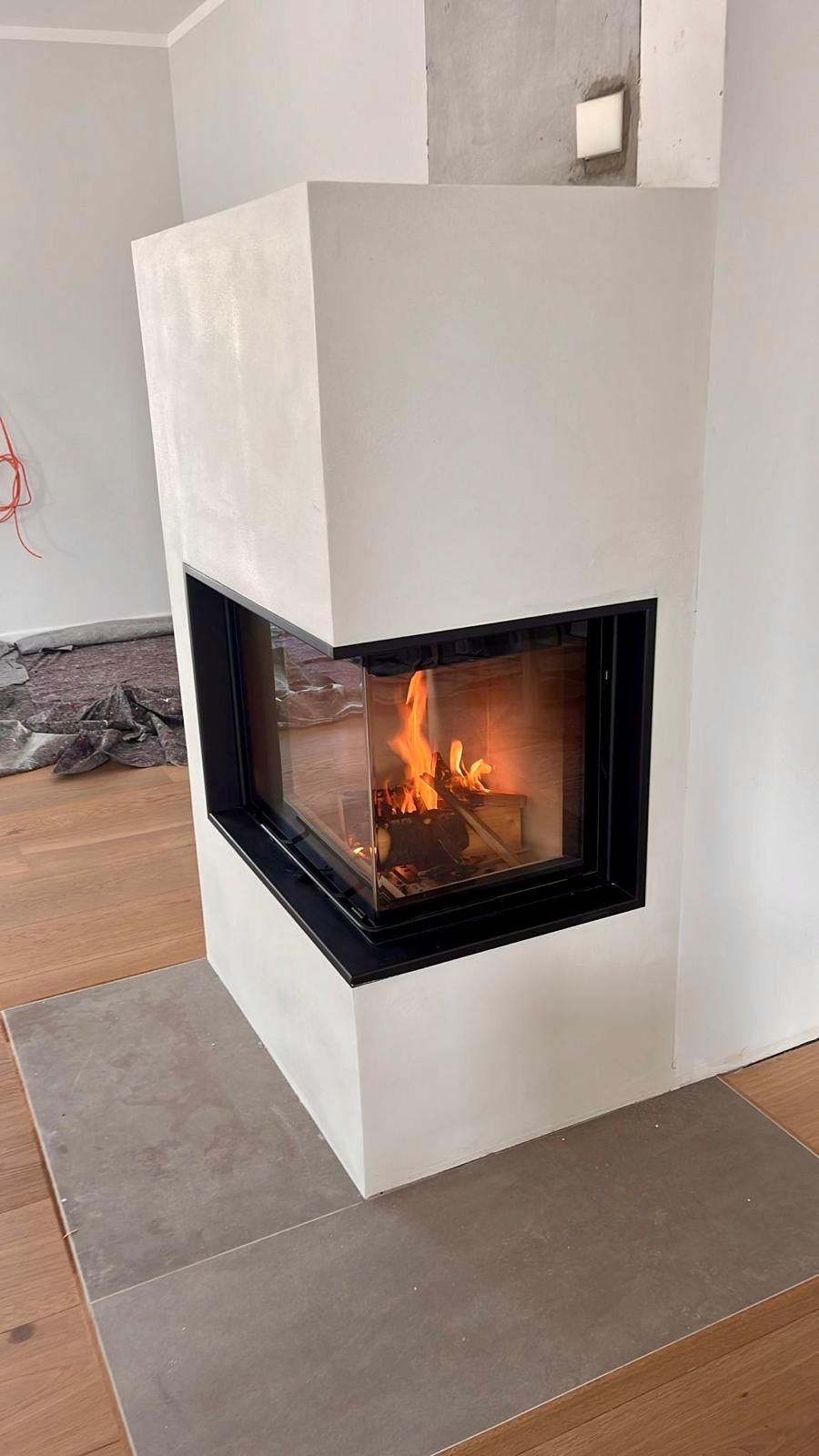 Moderner weißer Kamin mit brennendem Feuer vor hellen Wänden mit dunklem Rahmen.