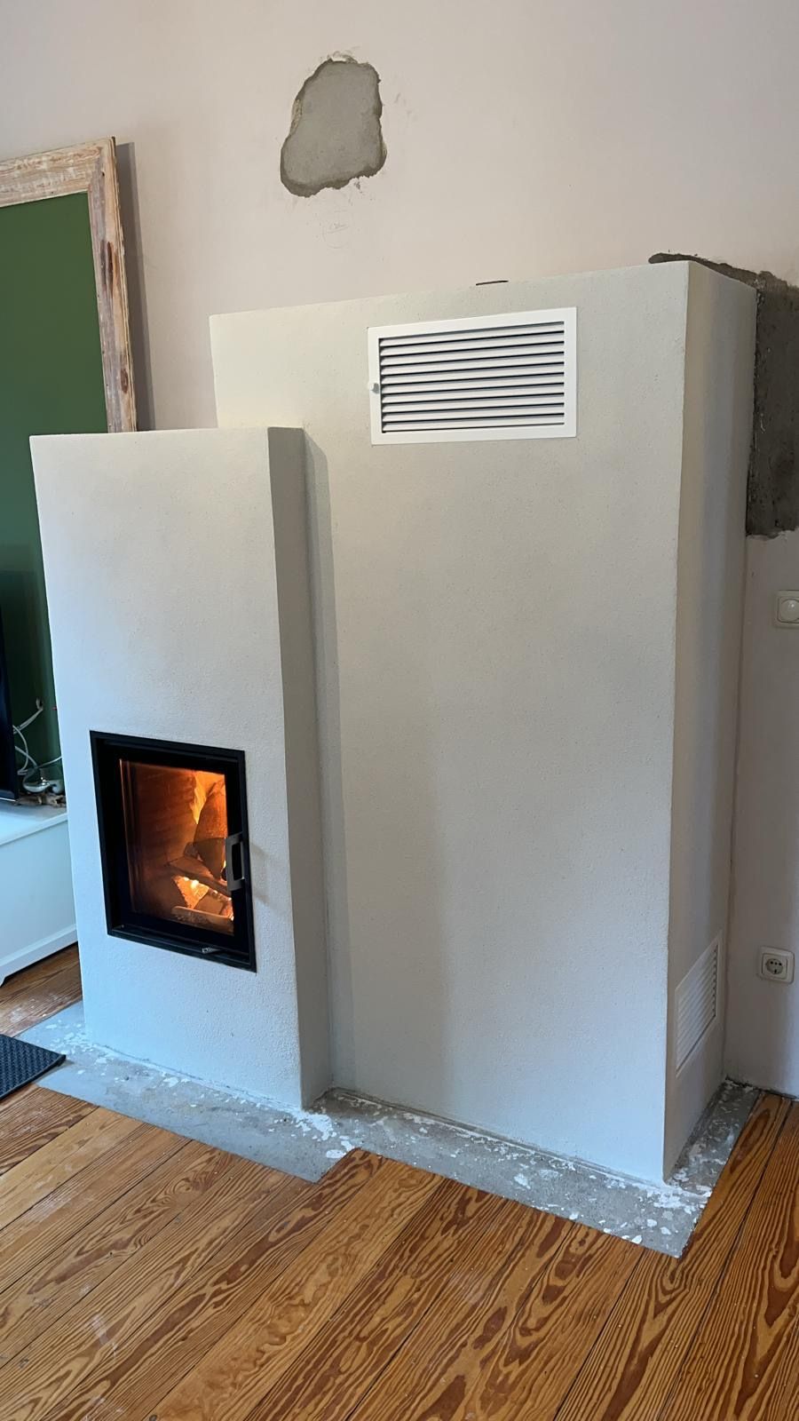 Hellgrauer, rechteckiger Kamin mit sichtbarem Feuer, Lüftungsöffnung und Holzboden.