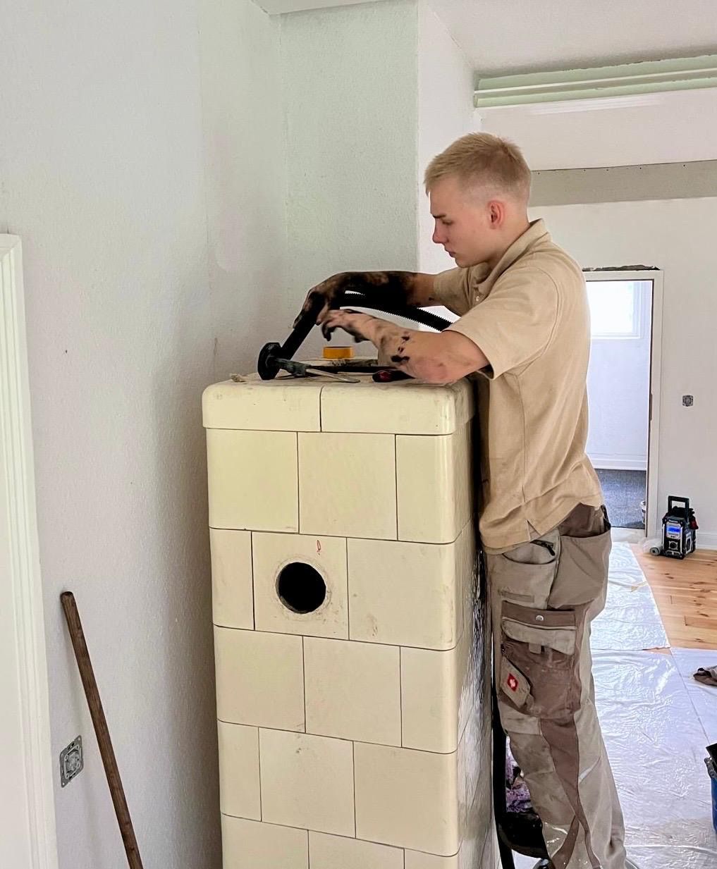 Ein Mann montiert einen Schornstein an einem weißen Backsteingebäude. Helle Arbeitskleidung, Innenaufnahme.